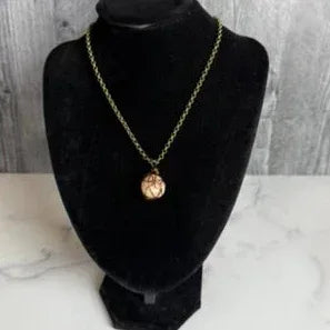 Bronze necklace with a pendant on a black mannequin bust against a marble and wooden background