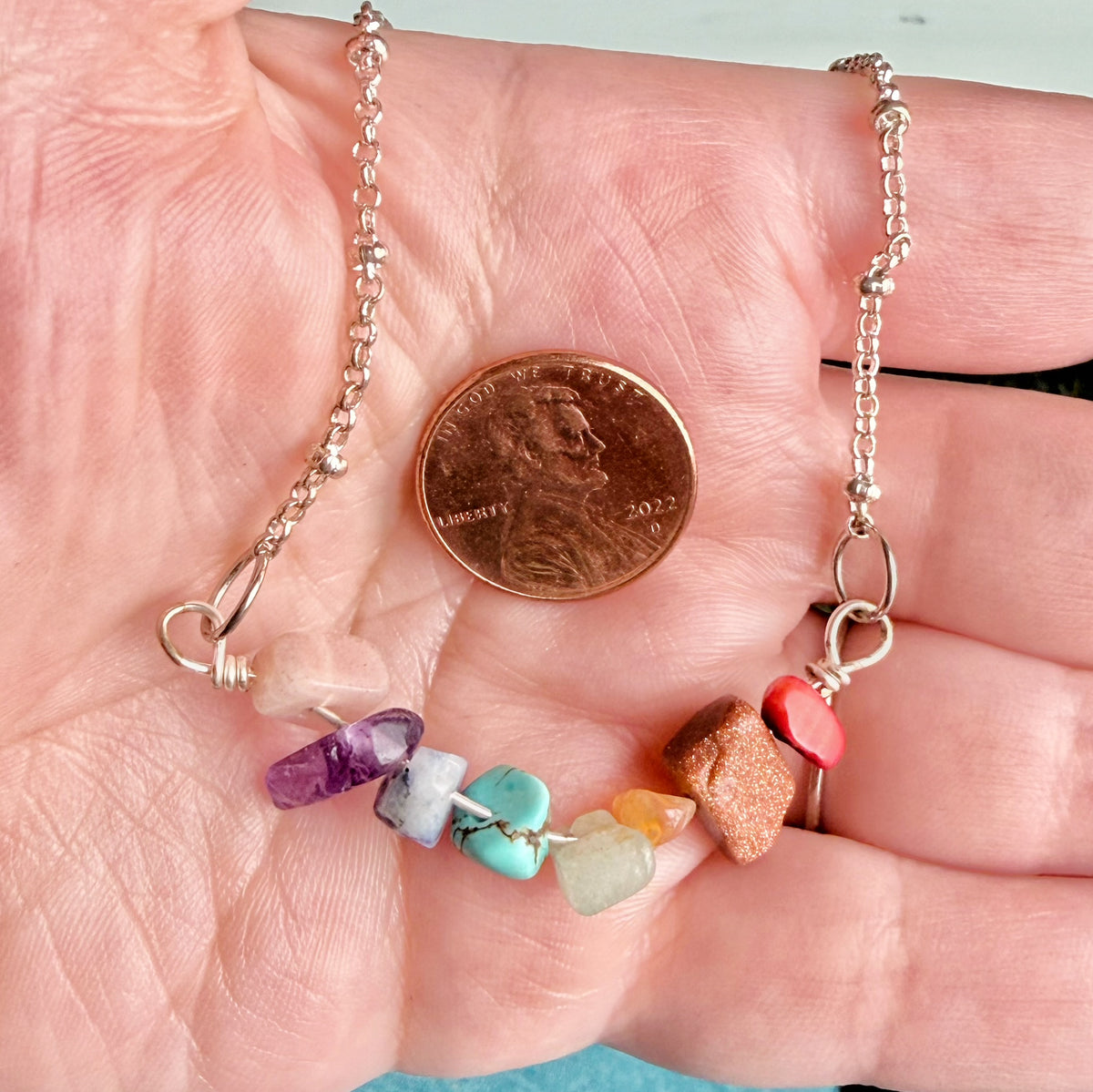 A close-up of a silver chain necklace draped across a person's palm, with a U.S penny for scale
