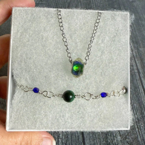 a jewelry set in a white box held by a hand, with a gray wooden background.