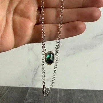 Small necklace with a pendant held between fingers on a marble surface