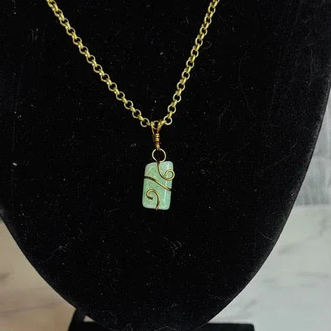 Gold chain necklace with a green pendant on a black velvet bust against a marble background