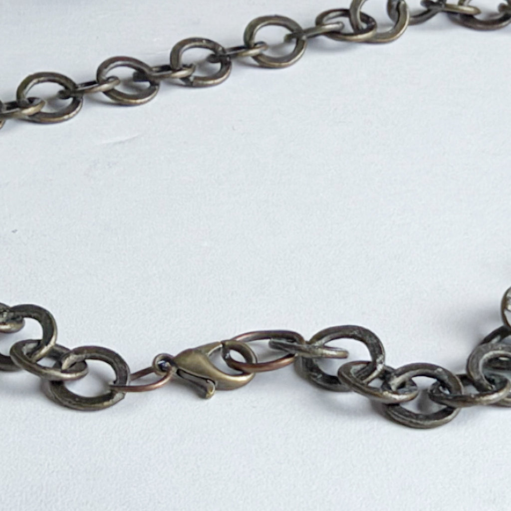 A close-up of a dark metallic chain necklace with a lobster clasp, laid on a light gray background.