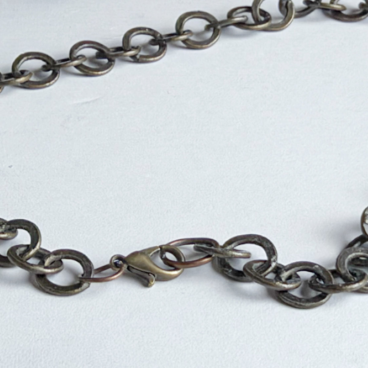 A close-up of a dark metallic chain necklace with a lobster clasp, laid on a light gray background.