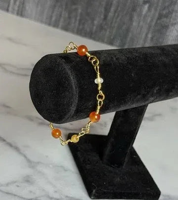 Gold bracelet with orange beads on a black velvet stand against a marble background