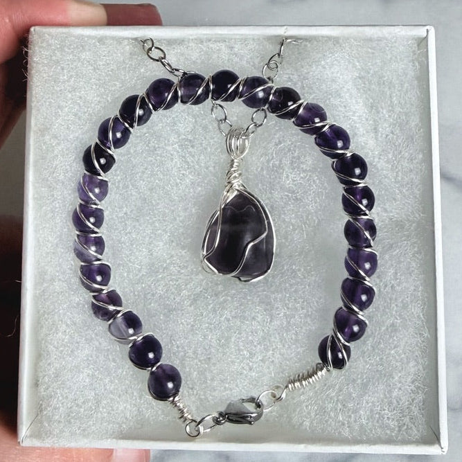 Amethyst bracelet and pendant set in a box held by a hand on a marble surface