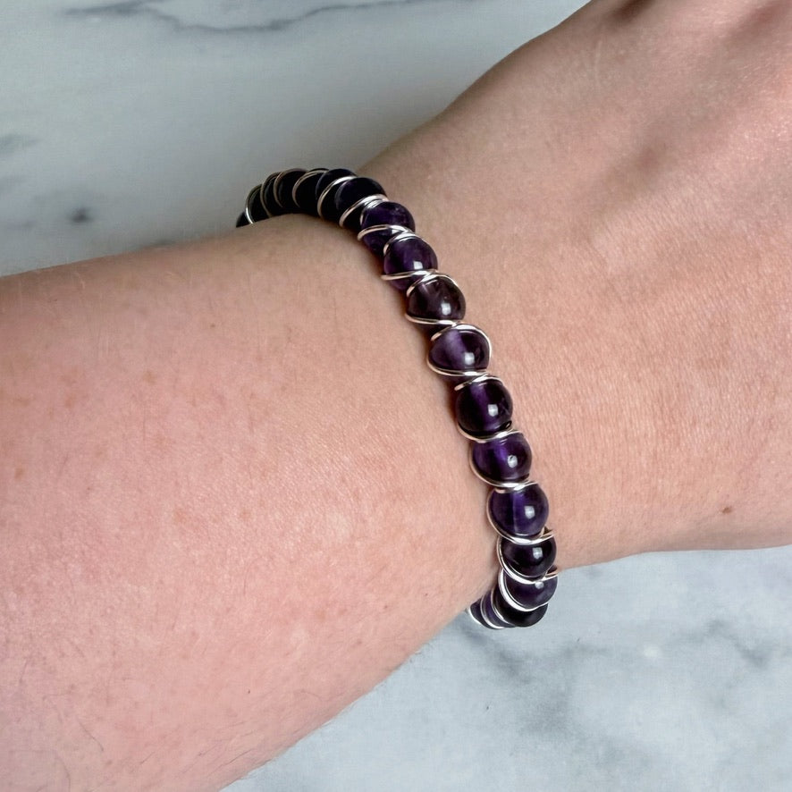 Purple beaded bracelet on a wrist with a marble background