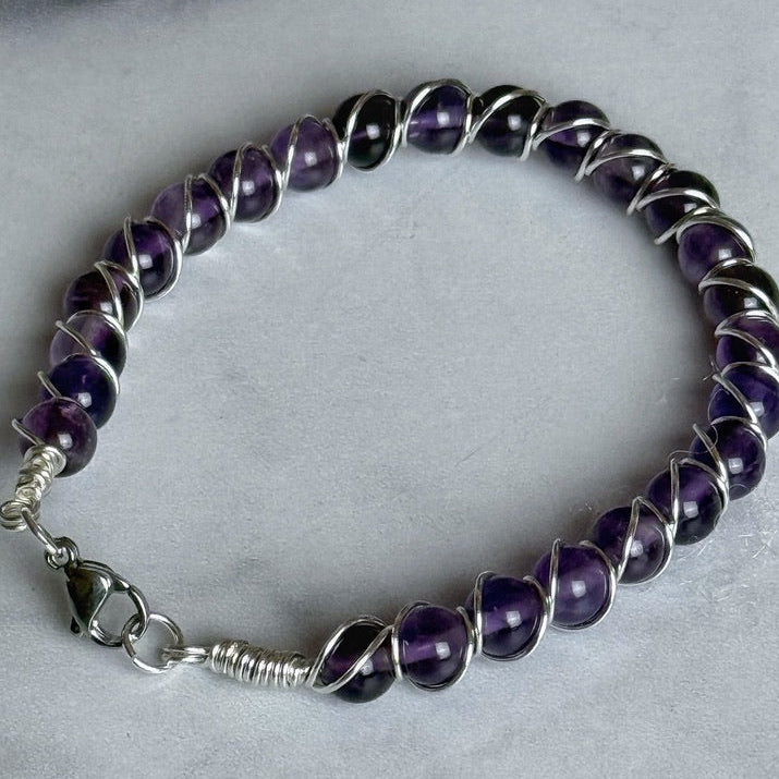 Amethyst beaded bracelet with silver clasp on a light gray background