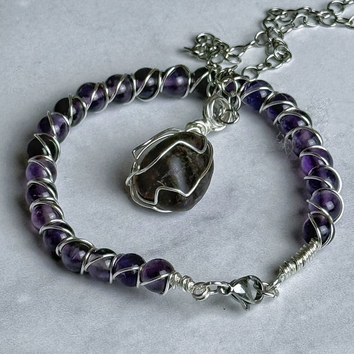 Purple beaded bracelet with a silver charm on a gray surface