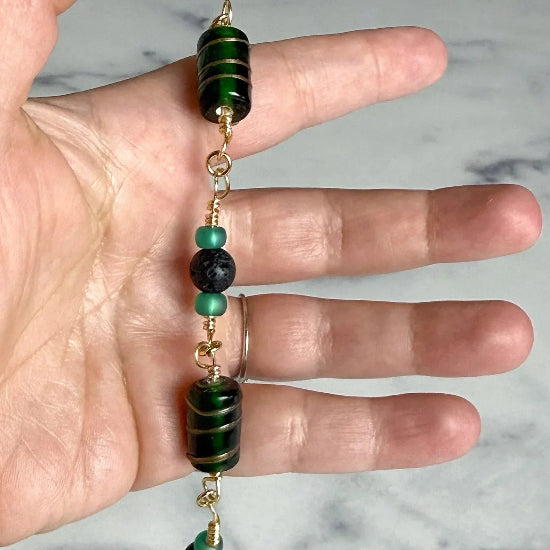 Hand holding a bracelet with green and black beads against a marble background