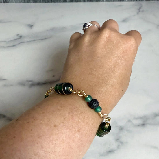 Hand wearing a bracelet with green and black beadson a marble surfaced 