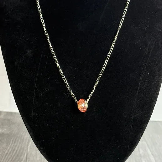 Necklace with an orange pendant on a black velvet bust against a white background