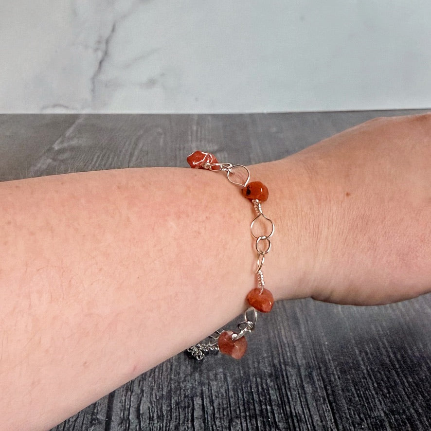Bracelet with red stones on a wrist against a gray background