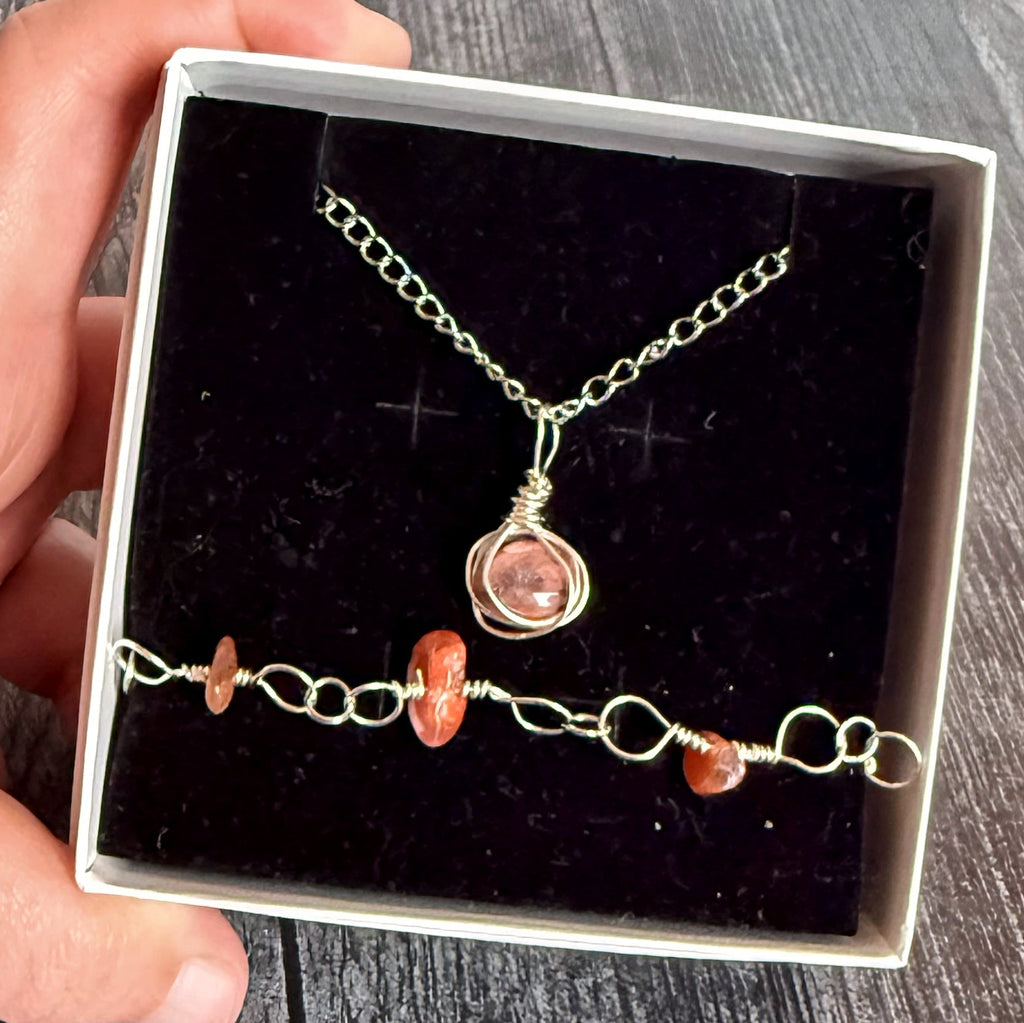 Hand holding a jewelry set with a necklace and bracelet in a box on a wooden surface