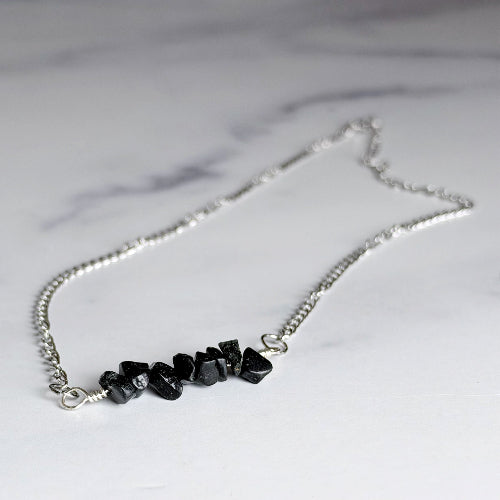 A silver chain necklace featuring a cluster of small, irregular black gemstones, displayed on a light gray marble surface.