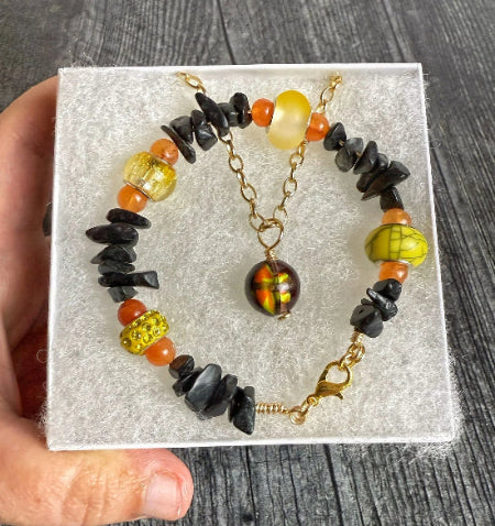 Beaded bracelet with black, orange, and yellow beads on a clear stand against a wooden background