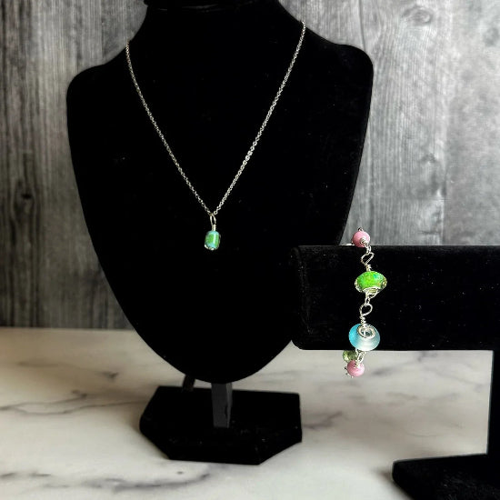 Necklace and bracelet on black mannequin stands against a wooden background