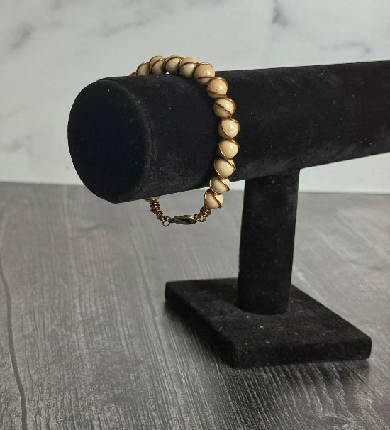 Bracelet with tan beads and copper wire wrapping on a black stand against a marble background