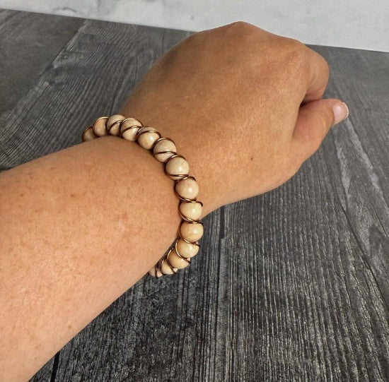 wrist wearing a tan beaded bracelet with wire wrapping on a dark wooden surface