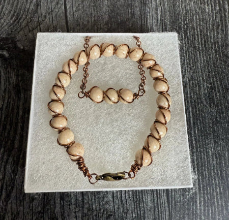 Necklace and bracelet set with beige beads and copper accents on a white card.