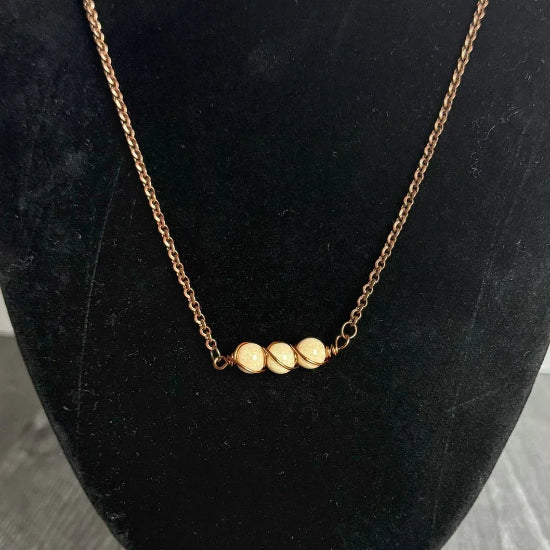 tan necklace on a black mannequin bust against a marble background