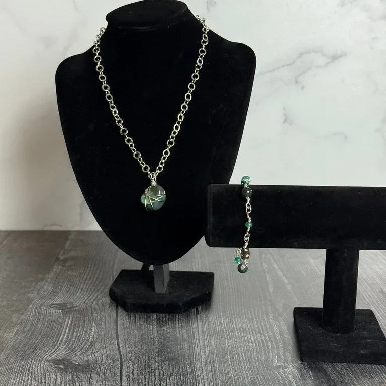 Necklace and bracelet on black stands against a marble background