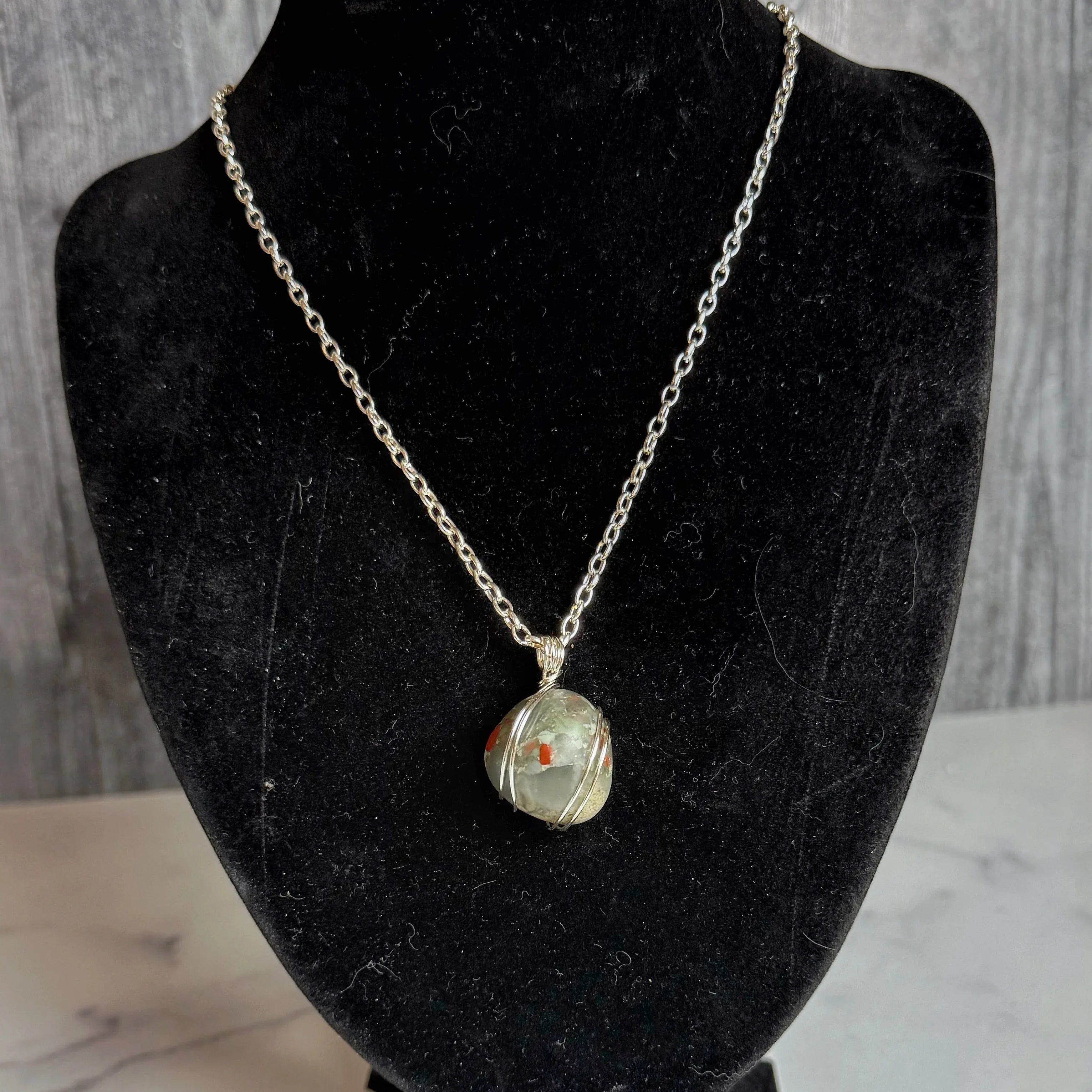 Necklace with a bloodstone pendant on a black velvet bust against a gray background
