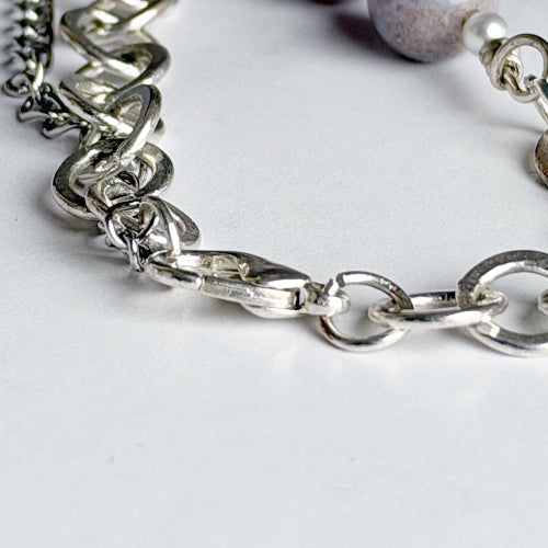 Close-up of a silver chain bracelet with polished interlocking links and a lobster clasp on a light gray background.