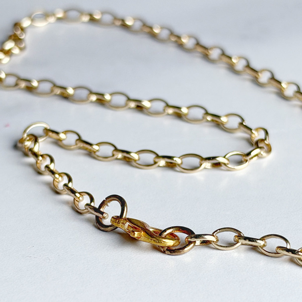 A close-up of a gold chain necklace with oval links and a lobster clasp, photographed on a plain light background.