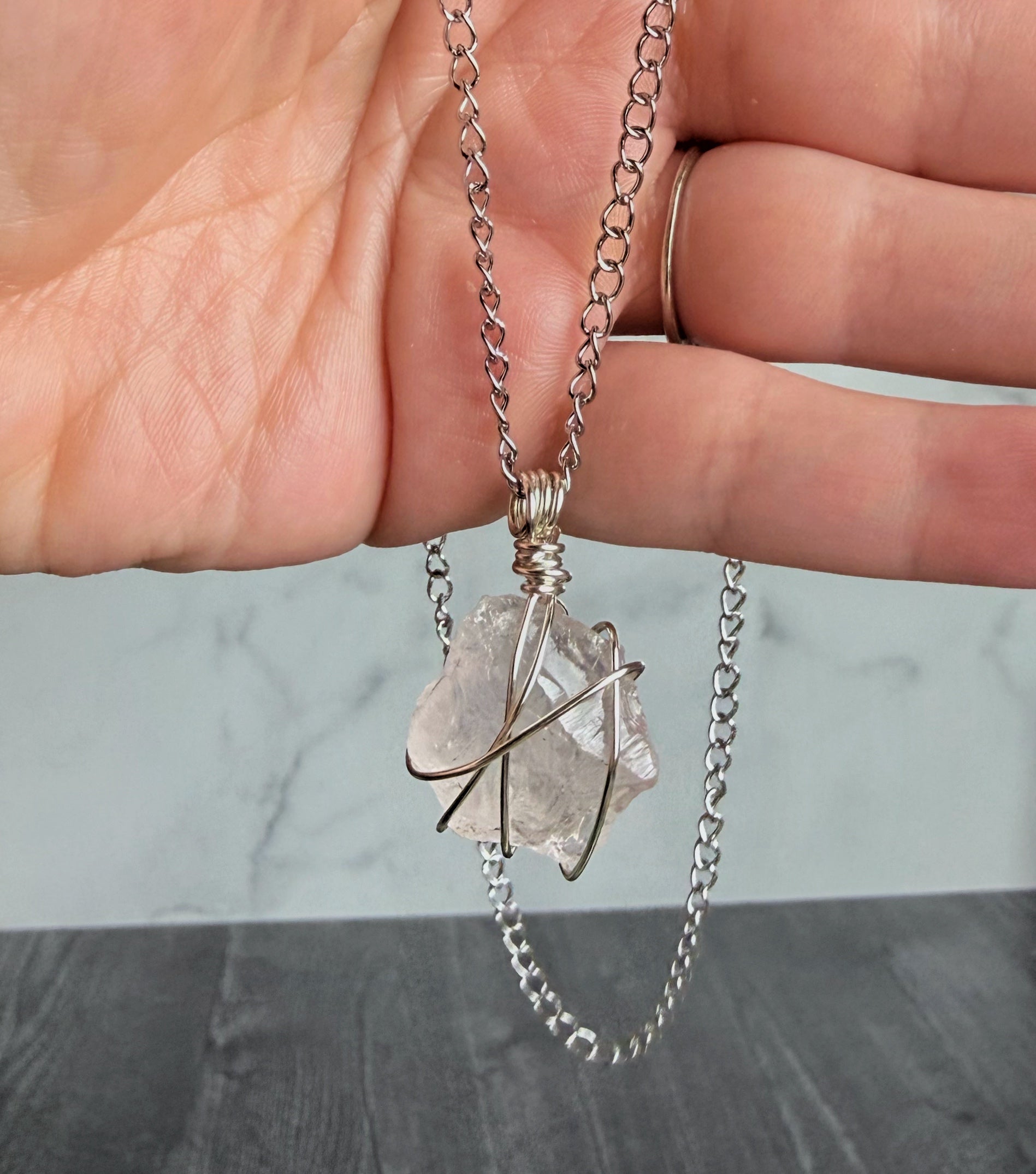 Necklace with a clear crystal pendant held by a hand against a neutral background