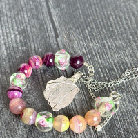 Beaded bracelet with floral designs and a silver leaf pendant on a wooden surface