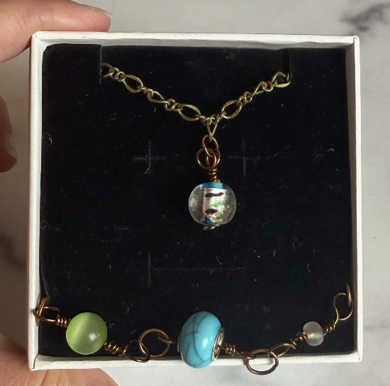 Multicolored necklace and bracelet in a boxheld in a box against a marble background