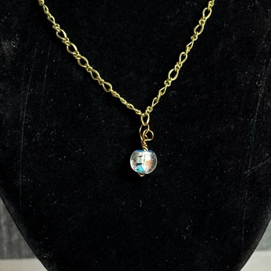 Gold chain necklace with a pendants on a black velvet stand against a wooden background