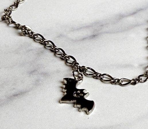 Silver chain bracelet with a black bat charm on a marble surface