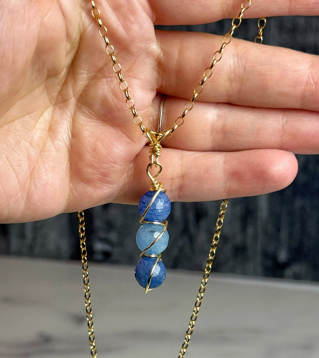 Gold necklace with blue stones held in a hand against a blurred background