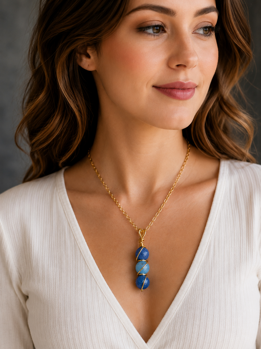 Woman wearing a gold necklace with blue stones against a neutral background