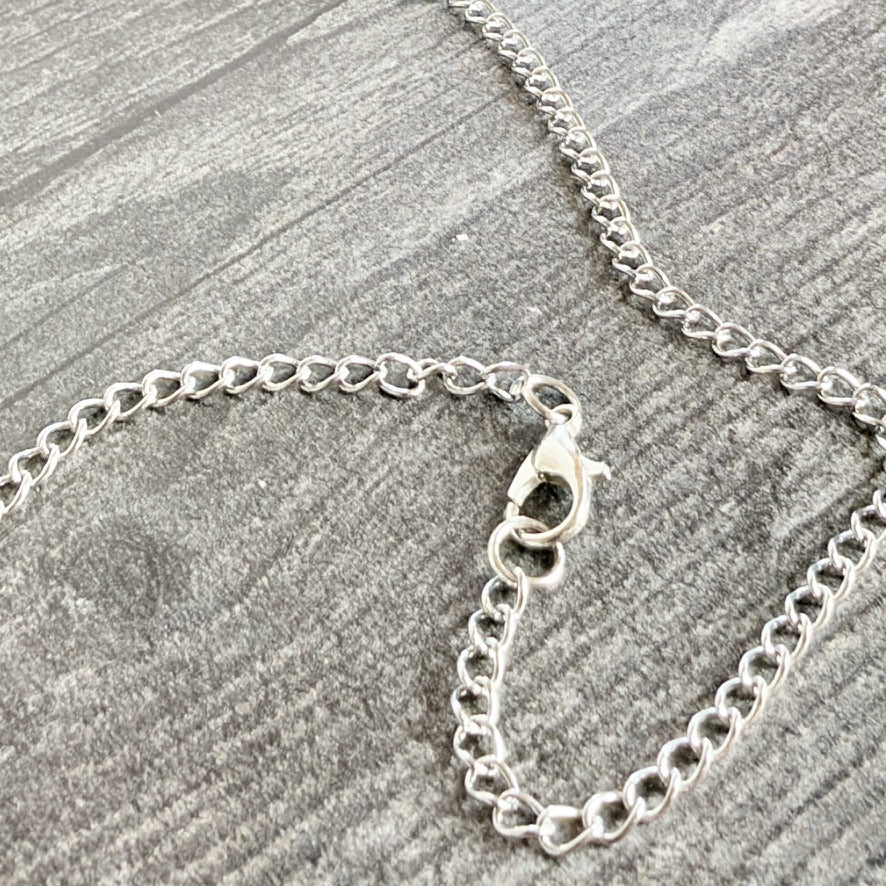 A close-up of a silver chain necklace with a lobster clasp, laid on a textured gray wood surface.