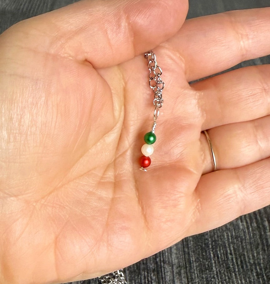 Hand holding a small necklace with three colored beads on a neutral background