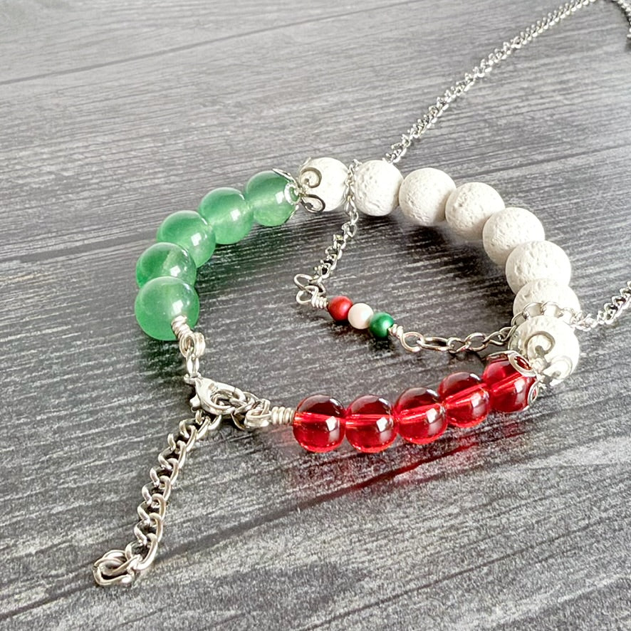 A silver chain bracelet with multiple beaded sections, including green translucent beads, white textured round beads, a red translucent bead section, and a small red, white, and green accent bead, displayed on a gray wood-textured background.