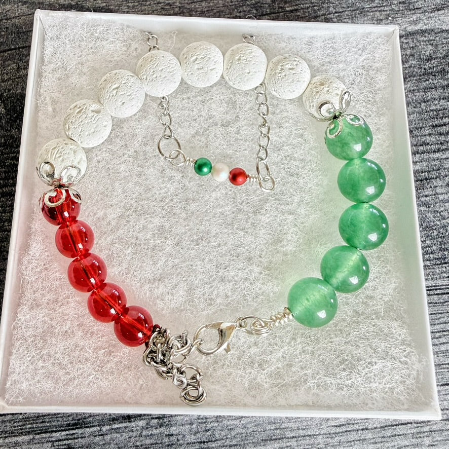 A beaded bracelet displayed inside a white gift box, featuring white textured round beads, a red section with glossy red beads, a green section with glossy green beads, and silver-tone chain and charm details.