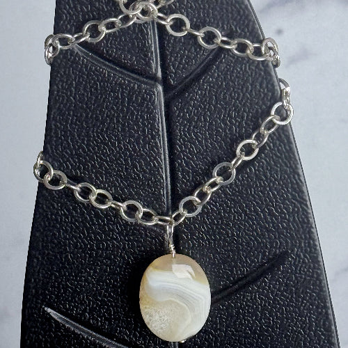 Silver chain necklace with a pendant on a black jewelry display