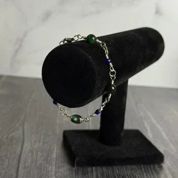 Bracelet with green and blue beads on a black velvet stand against a marble background