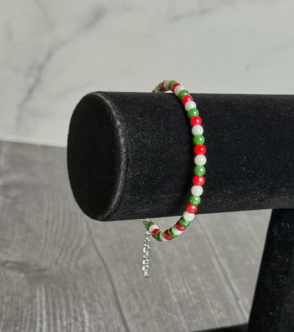 Beaded bracelet with red, green, and white beads on a black cylindrical stand against a gray background.