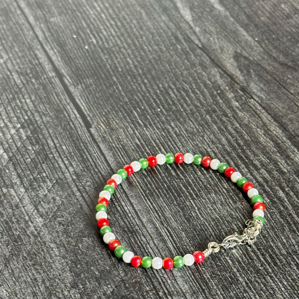 Beaded bracelet with red, green, and white beads on a dark wooden surface