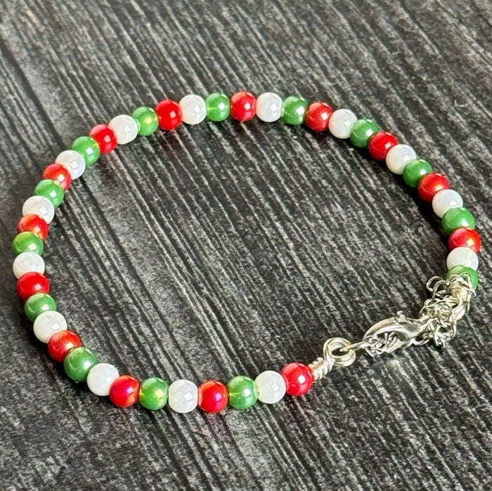 Beaded bracelet with red, green, and white beads on a dark wooden surface