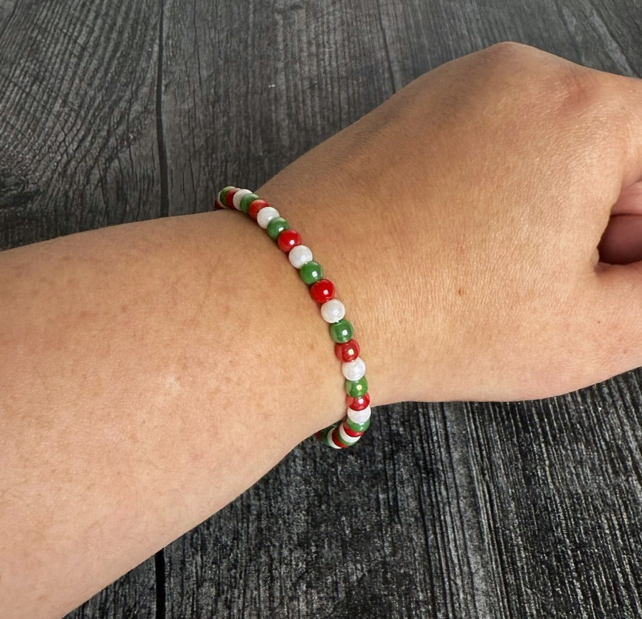 Beaded bracelet with red, green, and white beads on a wrist against a wooden background