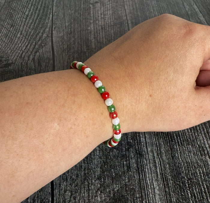 Beaded bracelet with red, green, and white beads on a wrist against a wooden background