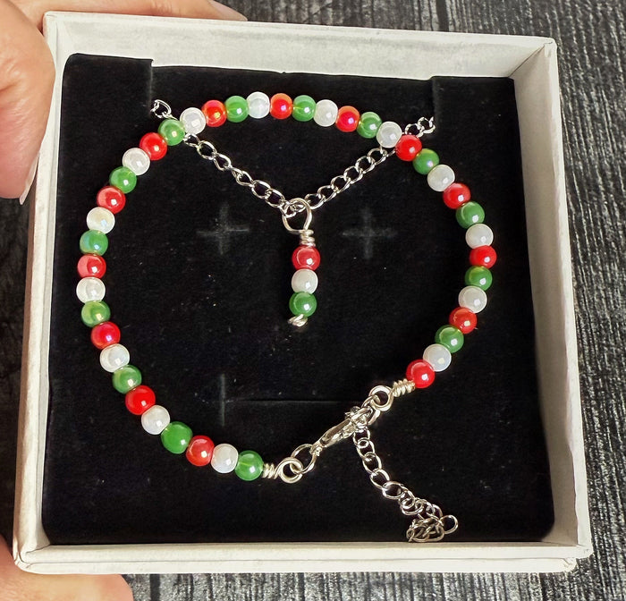 Beaded bracelet with red, green, and white beads in a box held by a hand on a wooden surface.