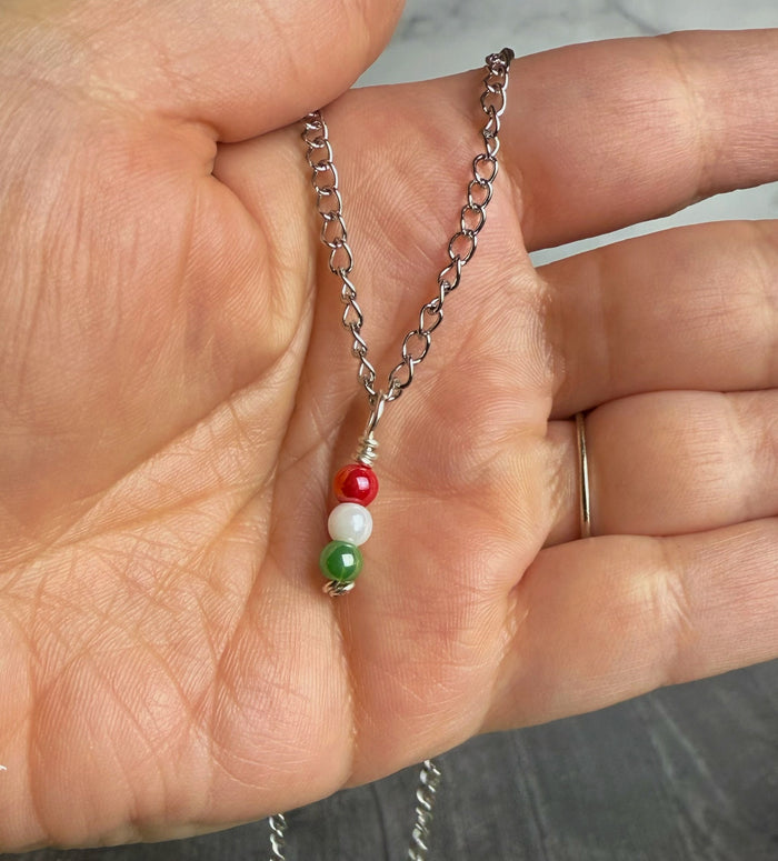 Hand holding a silver chain with red, white, and green beads.