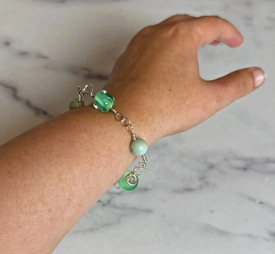 Hand wearing a bracelet with green beads on a marble background