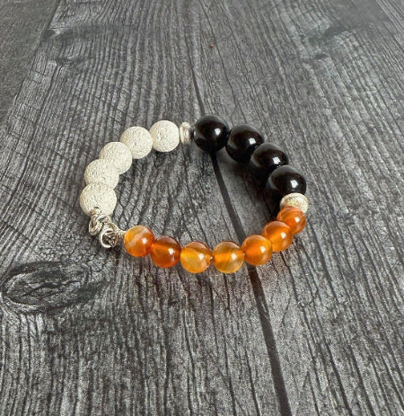 Beaded bracelet with orange, black, and silver beads on a wooden surface